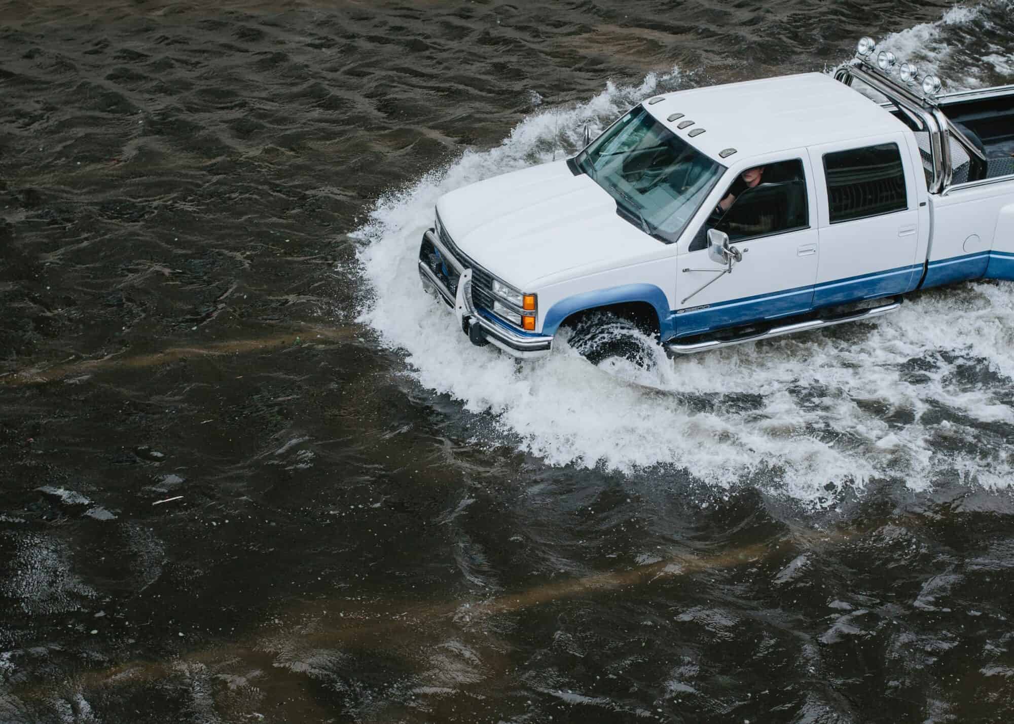 A pick up truck drives over a flooded a road.