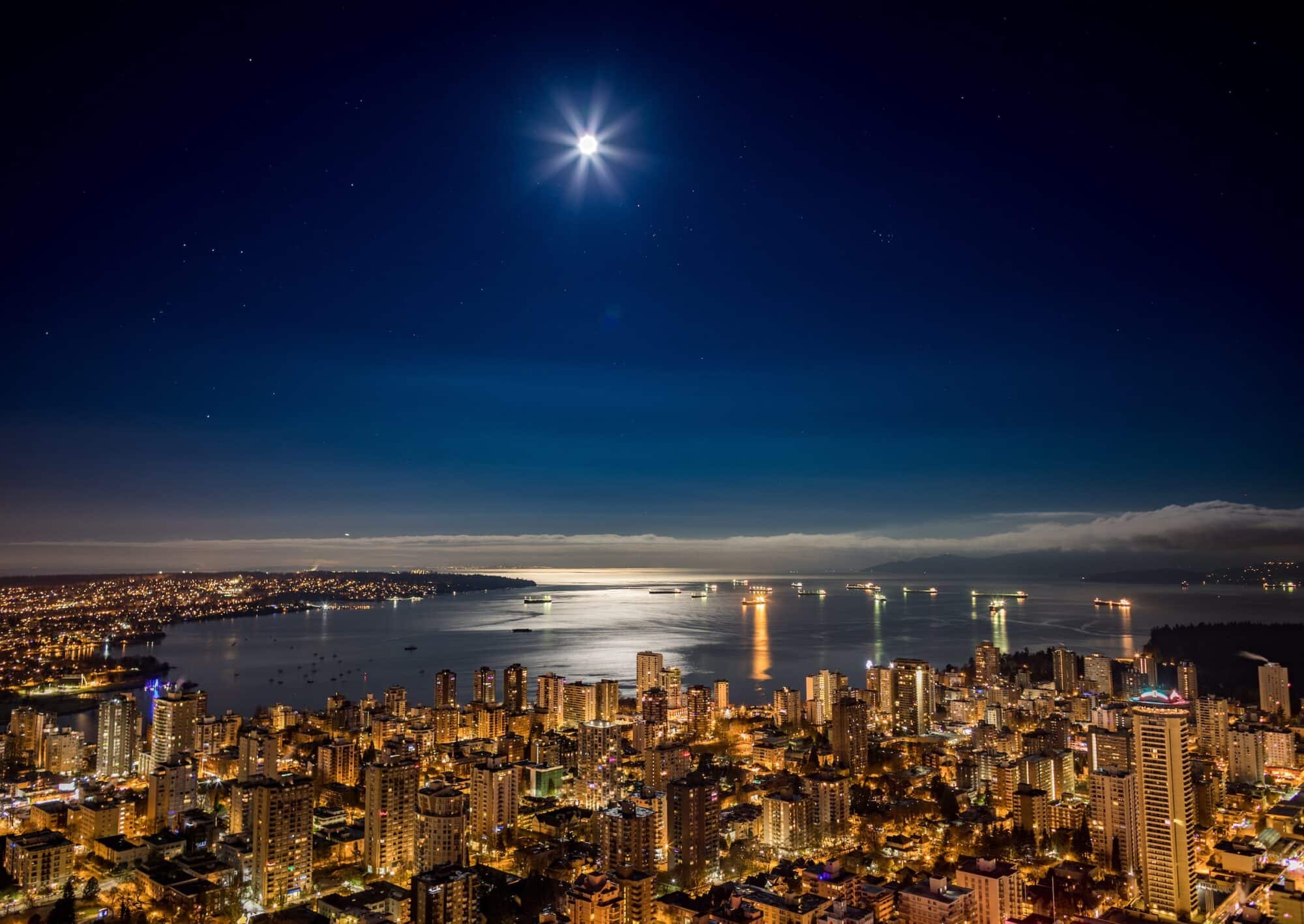 A view of downtown Vancouver lit up a night under moonlight looking over Burrard Inlet.