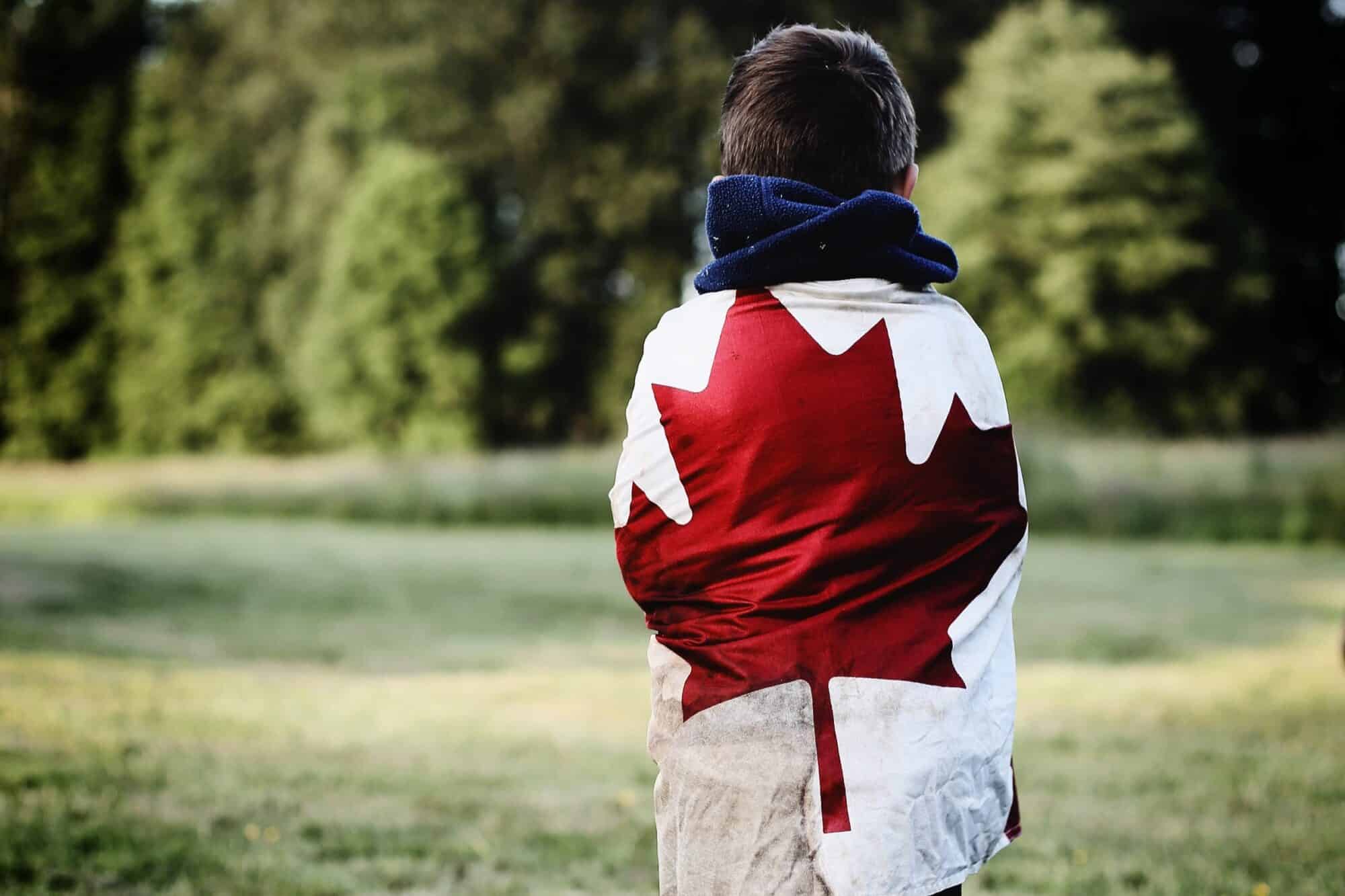 A Canadian child stands in a field draped in the Canadian flag.