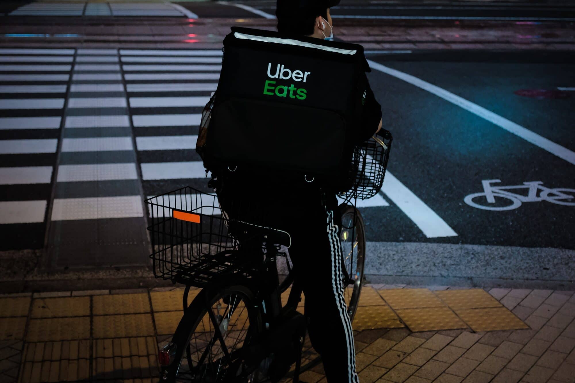 A bike courier with a Uber Eats backpack waits for the traffic signal before crossing the street at an intersection.