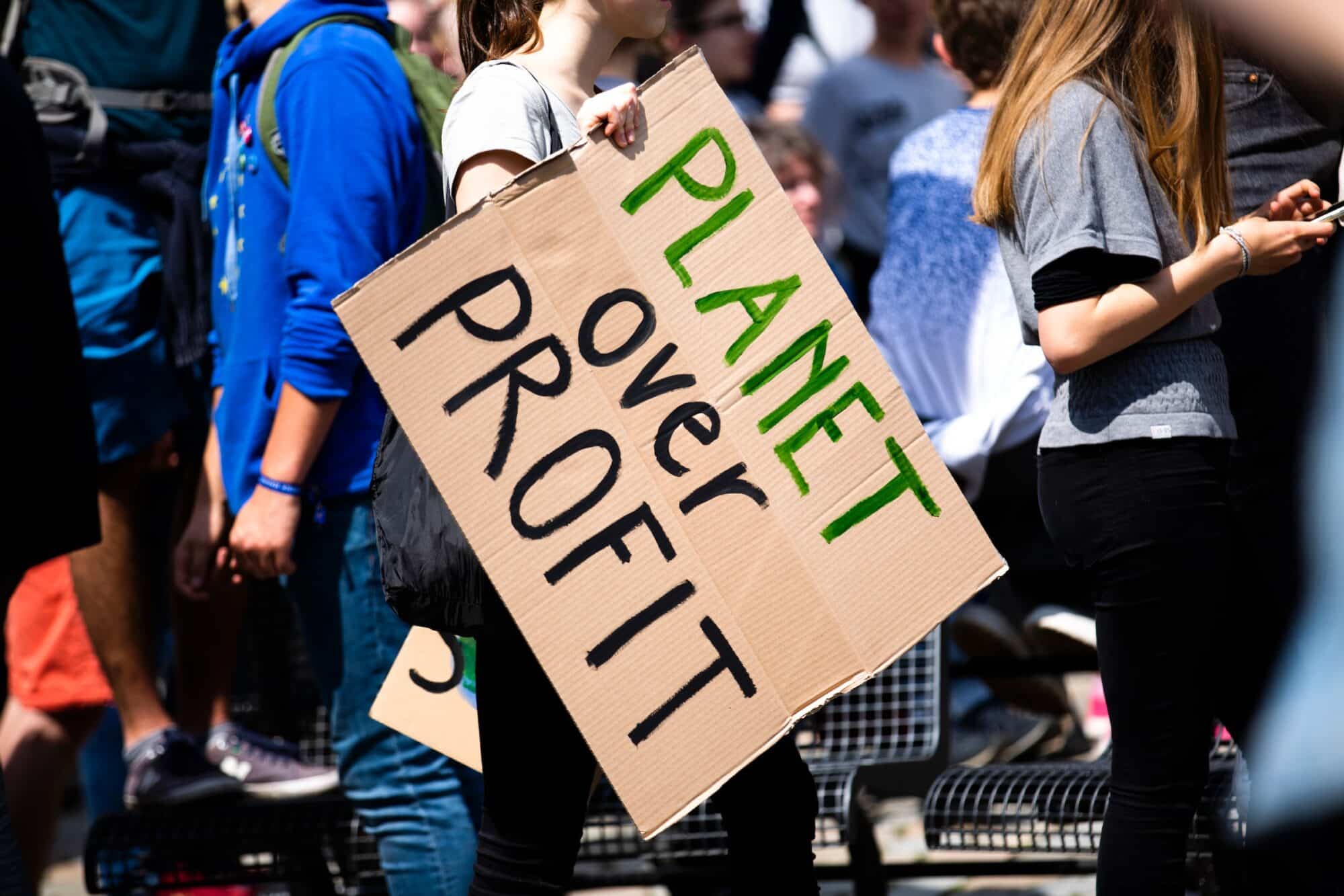 A climate protestor holds a cardboard sign that reads "plant over profit".