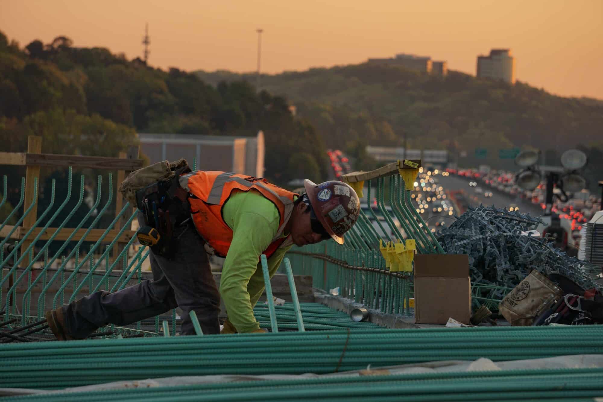 A construction worker builds infrastructure over a gridlocked highway.