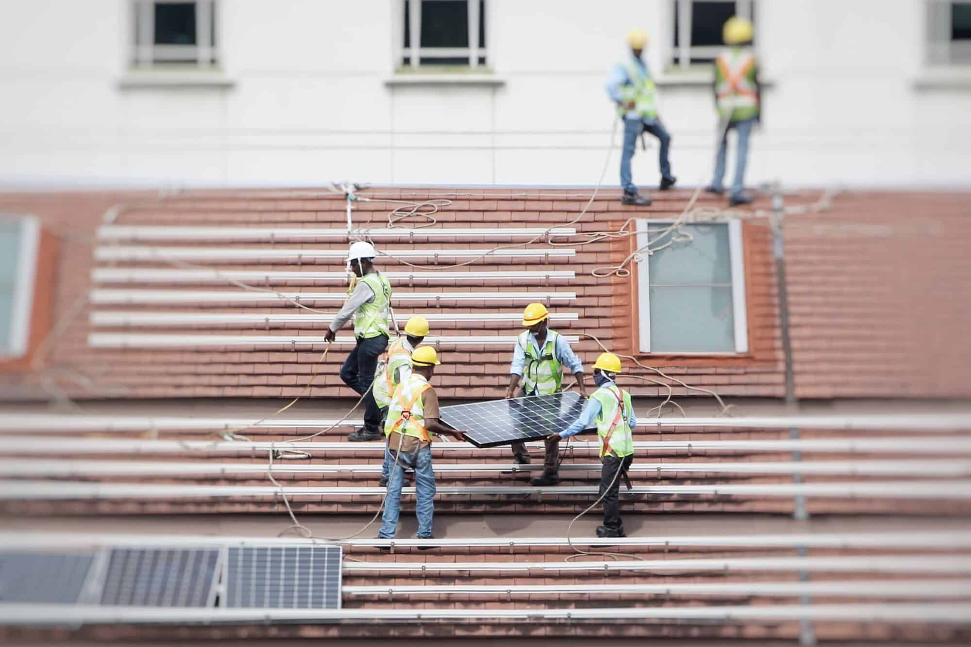A group of workers install solar panels on residential rooftops.