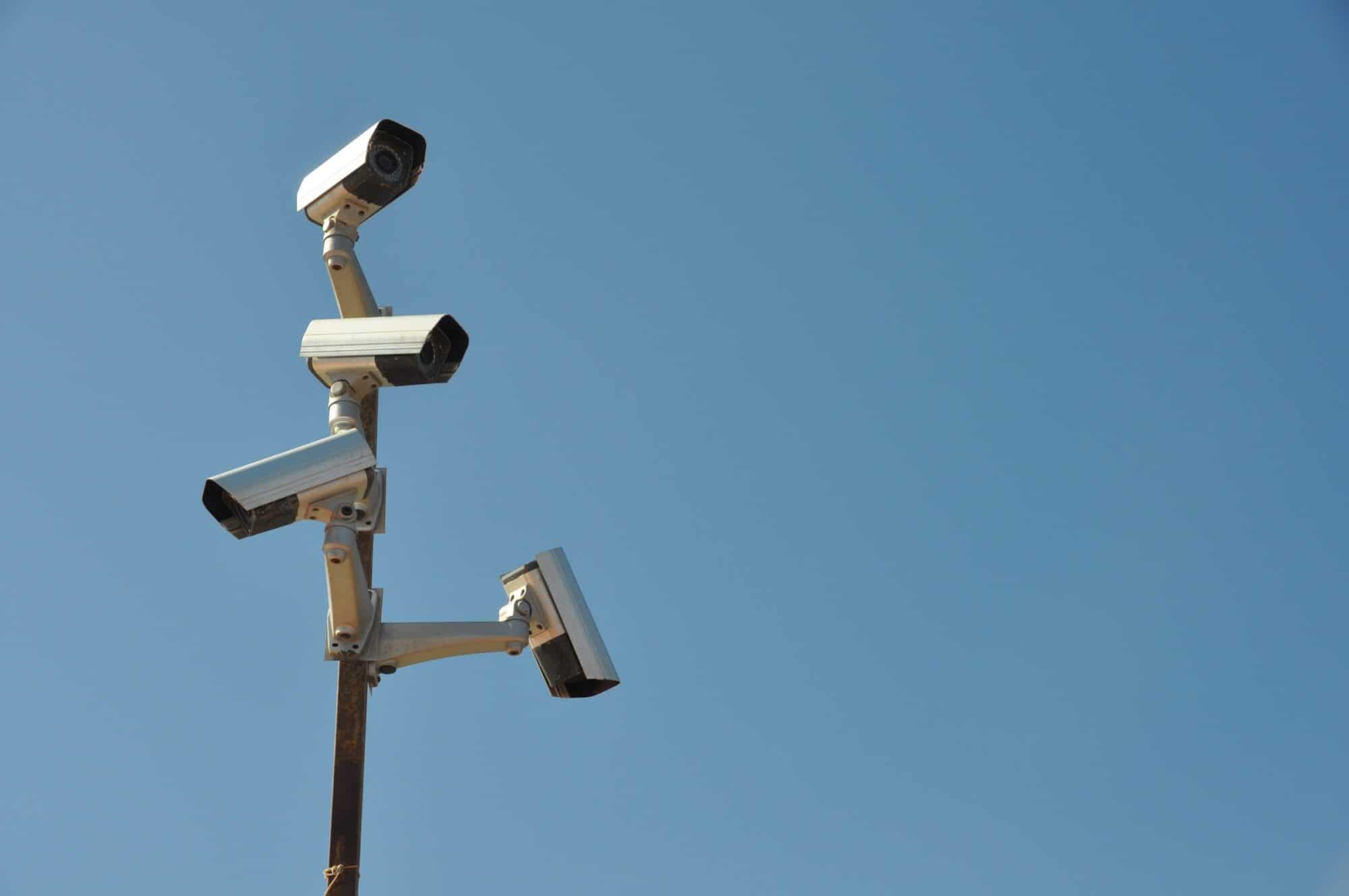 Four surveillance cameras pointed in different directions from a post against a blue sky.