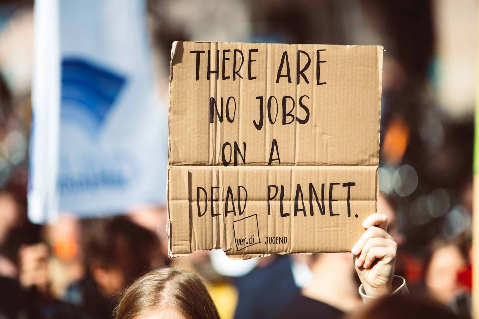 A climate protestor holds up a cardboard sign that says "There are no jobs on a dead planet."