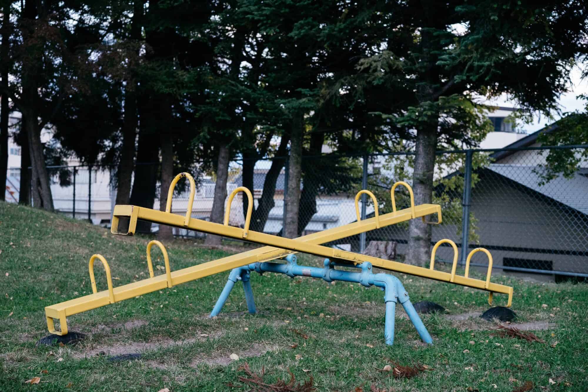 Two see-saws sit empty in a park.