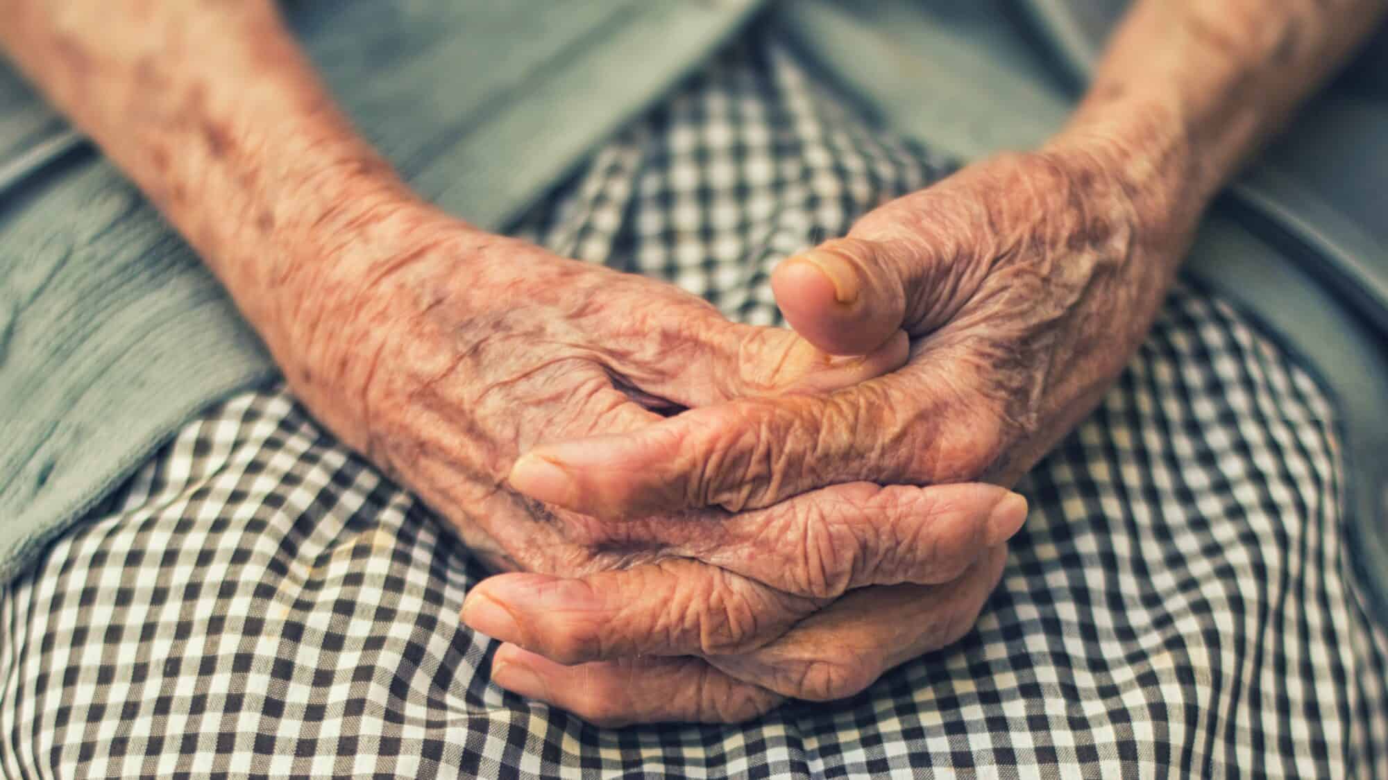 A pair of hands of an elderly person folded on their lap.