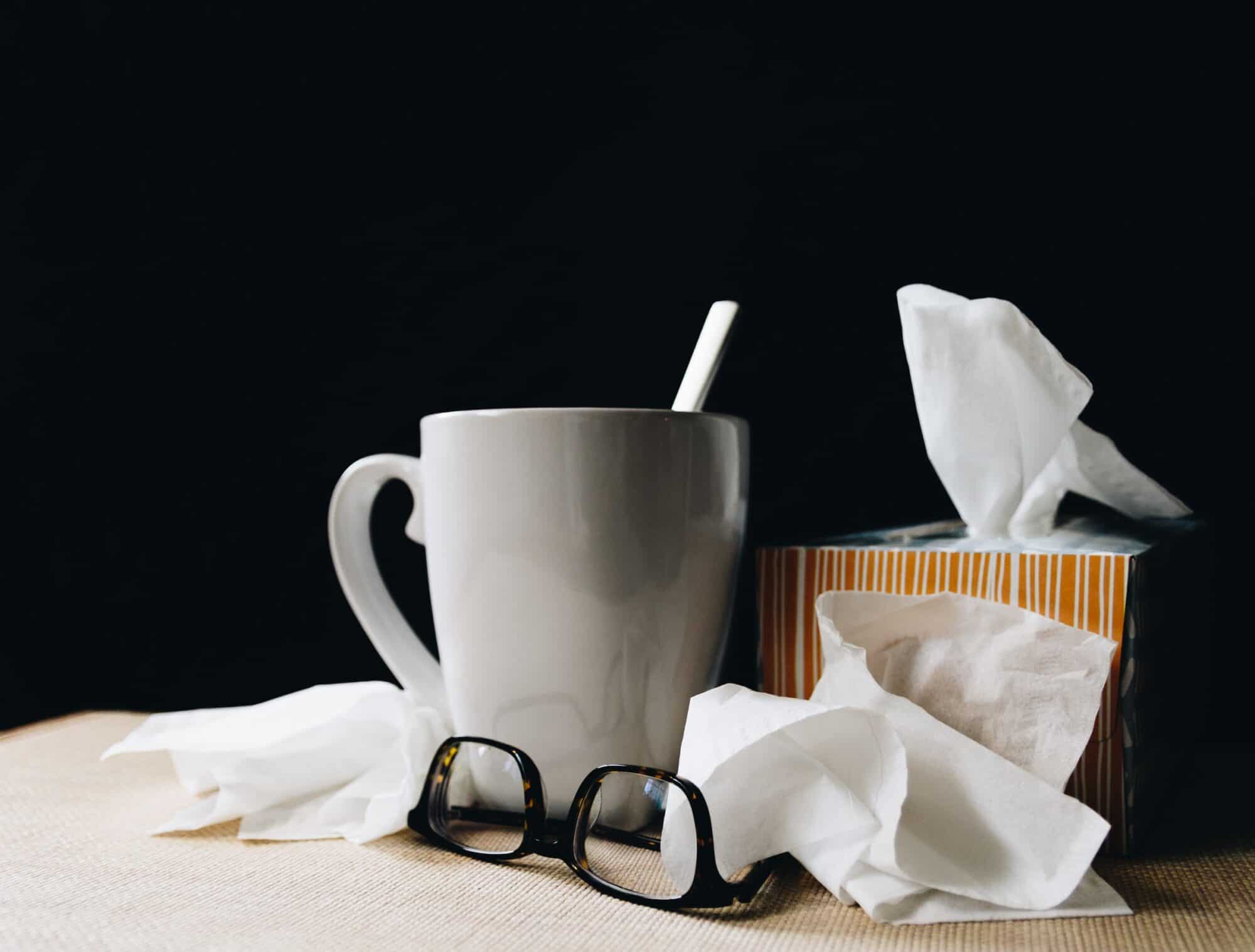 A mug of tea, used tissues, and a pair of glasses.