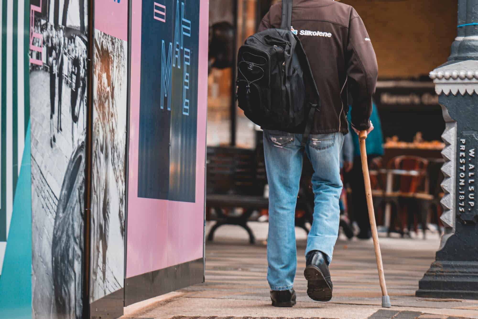 Man with a cane walking down a sidewalk.