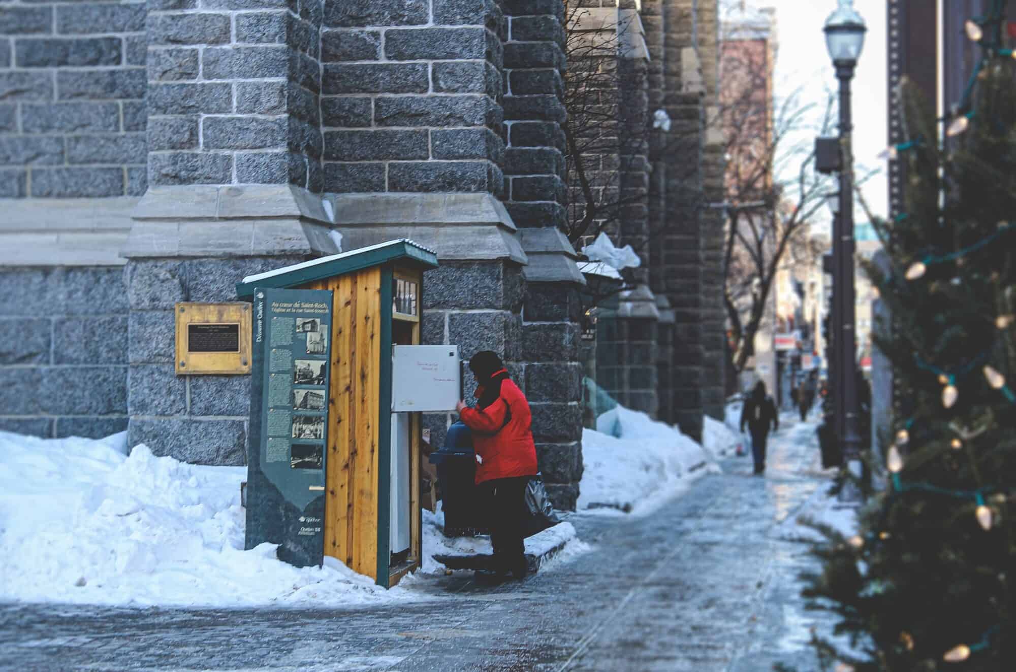 A person in need looks through a public fridge for food in the middle of a winter day.