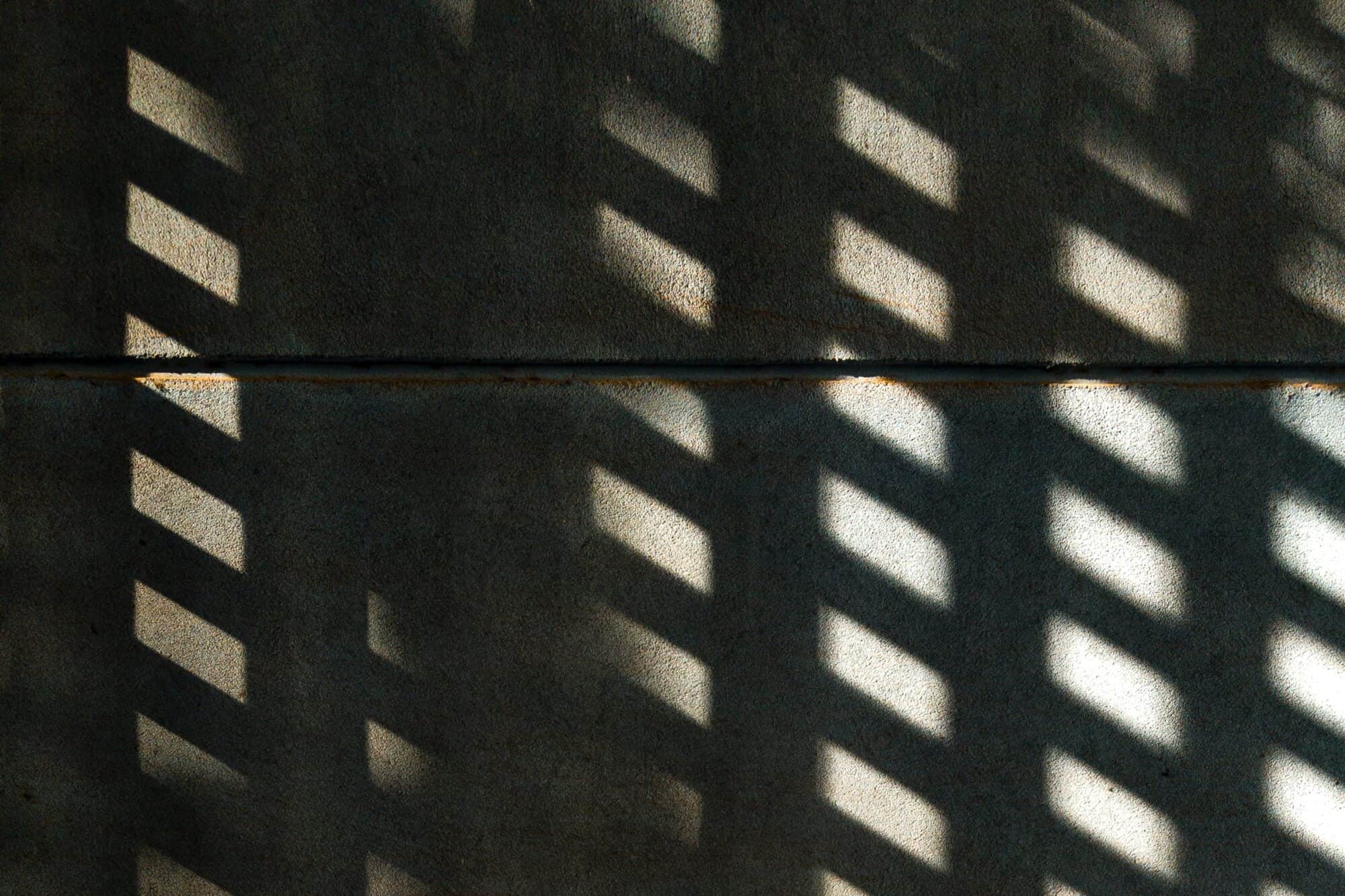 The shadows of bars over sunlight across a concrete wall.