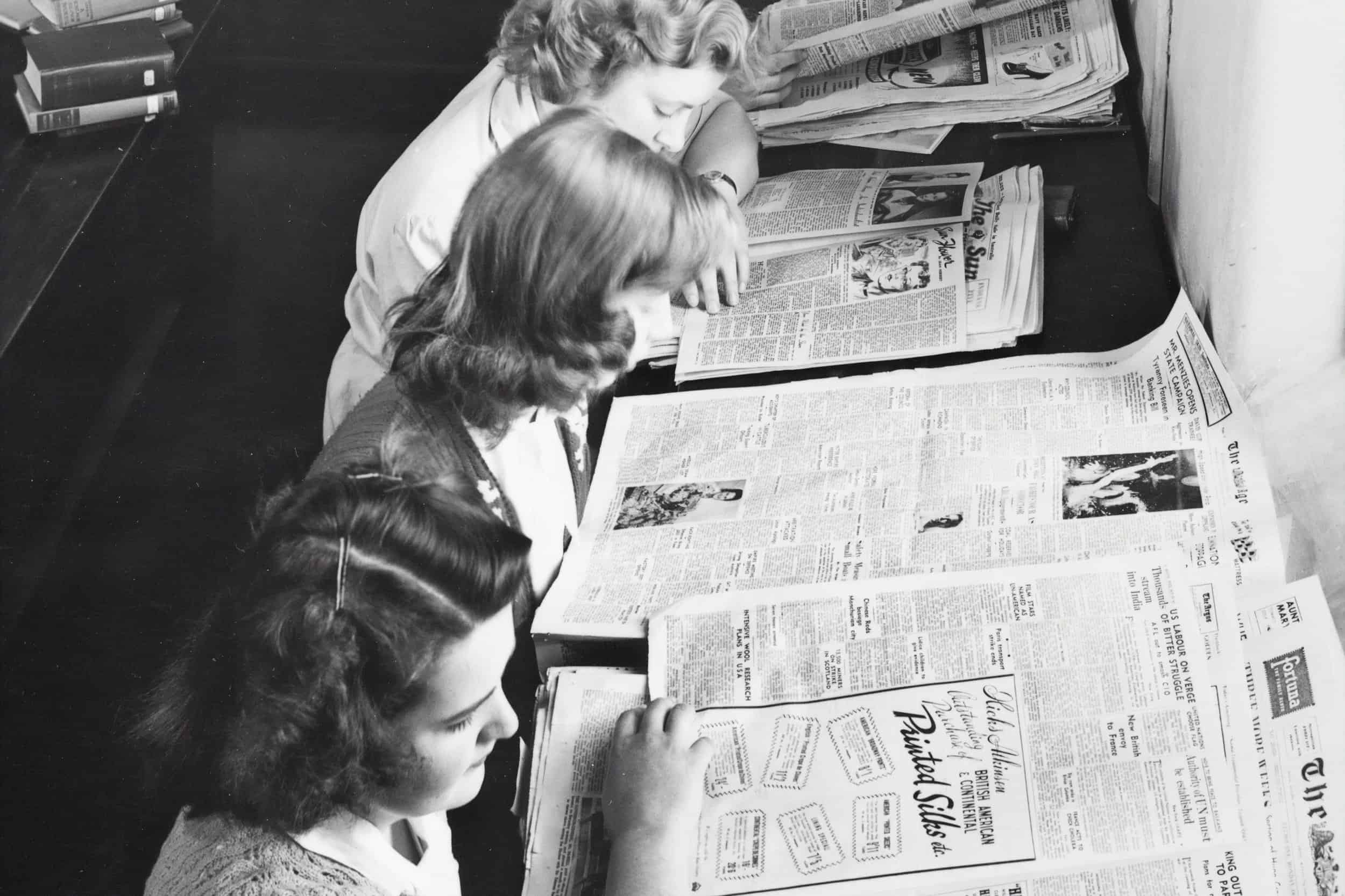 An old black and white photo of women reading newspapers at a library in the early 20th century.