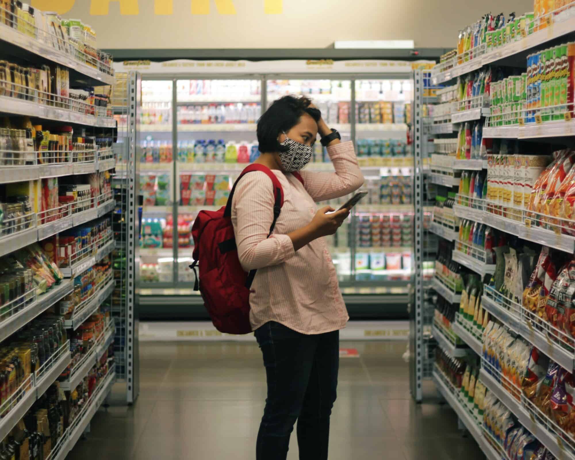 A masked woman looks distressed in the middle of a grocery aisle.